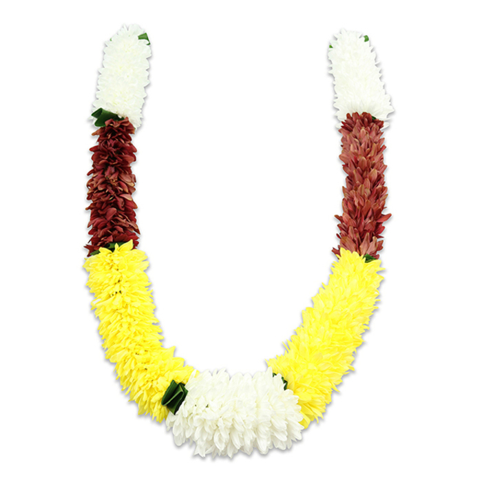 Set against a pure white field that casts a soft, defining shadow, this U-shaped floral garland presents a study in colour and texture familiar to any experienced florist in Beckton. Starting from each top end, the garland features tightly clustered, creamy white blooms-resembling small chrysanthemums or jasmine pompons-that give an ethereal, fluffy texture and signal auspiciousness. Immediately below, a rich maroon or reddish-brown band offers a deep, grounding contrast; the petals here are closely packed, creating a tactile, embroidered feel. The dominant lower segments are a long, continuous run of vivid yellow flowers, their round, plush faces arranged densely to produce a warm, glowing sweep across the bottom of the 'U'. At the lowest centre, the two yellow arms converge into a generous, gleaming cluster of pure white chrysanthemums that serves as the visual heart of the garland. Small dark-green leaf-like accents are thoughtfully placed at transition points-especially between the yellow and the bottom white cluster-adding restraint and a hint of natural foliage. Constructed from durable fabric petals and silk-like materials, the garland demonstrates close attention to hand-assembly: each petal is positioned to catch light and create subtle shadowing, so the whole reads as both lavish and orderly. In local practice around Gallions Reach and Prince Regent, such garlands are commonly chosen for temple offerings, pooja rituals, wedding ceremonies, and festival decorations like Diwali, where the white, yellow, and maroon palette conveys purity, prosperity, and devotion. The piece feels ceremonial yet approachable, a lasting expression of craft and cultural reverence prepared with the calm expertise of a neighbourhood florist.