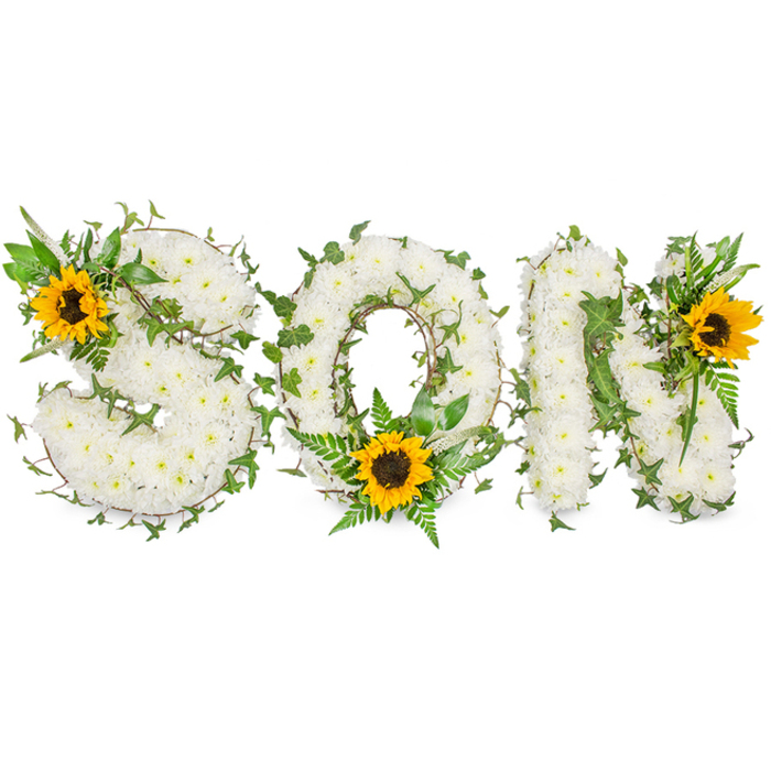 A meticulously composed memorial piece that spells out SON in strong capital lettering, set against a pure white studio background to allow precise inspection of materials and form. The base of each letter is densely covered with small white chrysanthemums, their tight, papery petals building a soft, pillowy texture that reads as both pristine and consoling. Winding through the white mass are rich, dark-green ivy vines whose glossy five-lobed leaves and sinuous stems anchor the composition and introduce a living, evergreen quality. Interspersed among the chrysanthemum field are lighter green fern fronds and pointed foliage that create layered depth and a delicate contrast of textures. Strategically placed sunflowers supply bold spots of colour: a large sunflower is set at the upper-left curve of the S, another is nestled at the lower center of the O amid fronds, and a third punctuates the upper-right side of the N. Each sunflower features broad, golden-yellow petals radiating from a distinct dark brown disk, giving the arrangement an uplifting visual rhythm against the predominantly white surface. The photograph's neutral background and soft directional lighting emphasise the composition's sculptural quality and the interplay of softness and structure, making this tribute suitable for articles about funeral floristry, bespoke remembrance pieces, or local memorial services in Beckton and nearby Cyprus or Prince Regent Lane.