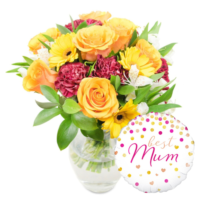 A generous, sunlit arrangement photographed on a white background: the composition centres on several large orange and yellow roses whose layered, spiralling petals convey a warm, uplifting energy, complemented by bright yellow gerbera daisies whose dark centres offer crisp visual contrast. Deep burgundy carnations add richness and texture with their tightly ruffled petals, creating shadows and depth between the brighter blooms. Interspersed among the heavier florals are sprays of white alstroemeria, their narrow petals and faint speckling bringing a refined, delicate perfume and a lightness of touch. The bouquet is cushioned by a mix of glossy broad leaves and fine green sprigs that give the overall silhouette a soft, verdant frame. Everything is held in a clear glass vase where the green stems and clean water are visible, the transparency signalling a recent arrangement and careful conditioning. To the lower right, partially overlapping the vase, a round white Mylar balloon adds a playful, celebratory note: it is dotted with scattered gold and fuchsia polka dots and tiny heart motifs, and carries the handwritten-style message best Mum in flowing hot-pink cursive. The whole ensemble reads as an intimate, joyful gift - ideal for Mother's Day, a birthday, or a thank-you - that would suit a doorstep in Beckton or a cozy living room near Gallions Reach Shopping Park. The bouquet's textures, colours, and scent profile make it an expressive choice for local flower delivery around Beckton and the Royal Docks.