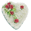 A gentle, heart-shaped funeral tribute built from a dense cushion of pure white chrysanthemums rests against a clean white backdrop, its surface like a soft, clouded pillow of tiny petals. The chrysanthemums create a seamless, textural field that speaks of quiet purity and calm, each bloom tightly placed to form the silhouette of a classic memorial heart. From the upper left a poignant cluster of three deep crimson roses rises, their velvety petals unfolding into full bloom and set amid glossy green foliage and feathery fern-like fronds; slender blades of bright green bear grass arc outward, giving the spray a whisper of motion as if breathed on by a soft wind. Two solitary red roses punctuate the composition - one near the upper right curve, the other at the lower point - each with minimal green accents that allow the intense, mournful crimson to hold the eye and suggest personal remembrance. A narrow emerald-green satin ribbon neatly trims the heart's edge, framing the white chrysanthemum bed with a refined, somber line that deepens the shape. Overhead lighting catches the roses' satin sheen and throws delicate shadows into the chrysanthemum's textured surface, heightening depth without ostentation. The scent is mild and comforting: green leaf top notes, the faint sweet musk of chrysanthemum, and the richer, velvety perfume of the roses. This arrangement reads as composed, reverent, and intimate - the kind of sympathy heart a Beckton family might choose for a chapel near Beckton Park or a service in the Royal Docks, offered with the attentive care of a local florist familiar with grieving neighbours and quiet farewells.